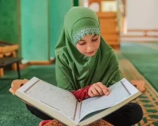 Child in green hijab reading Quran on carpet, promoting Islamic education and devotion Online Quran Courses